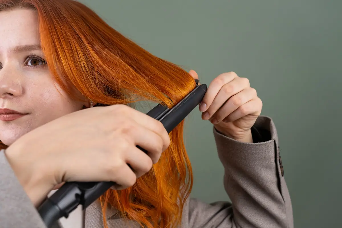 Close-up of a flat iron gliding through long copper-red hair